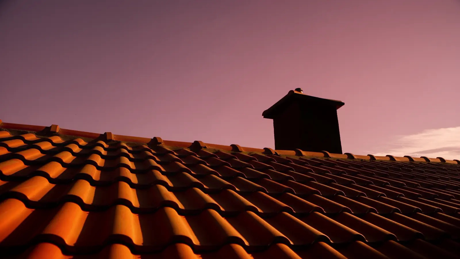 Dachziegel mit Kamin im Abendlicht, der Himmel färbt sich violett