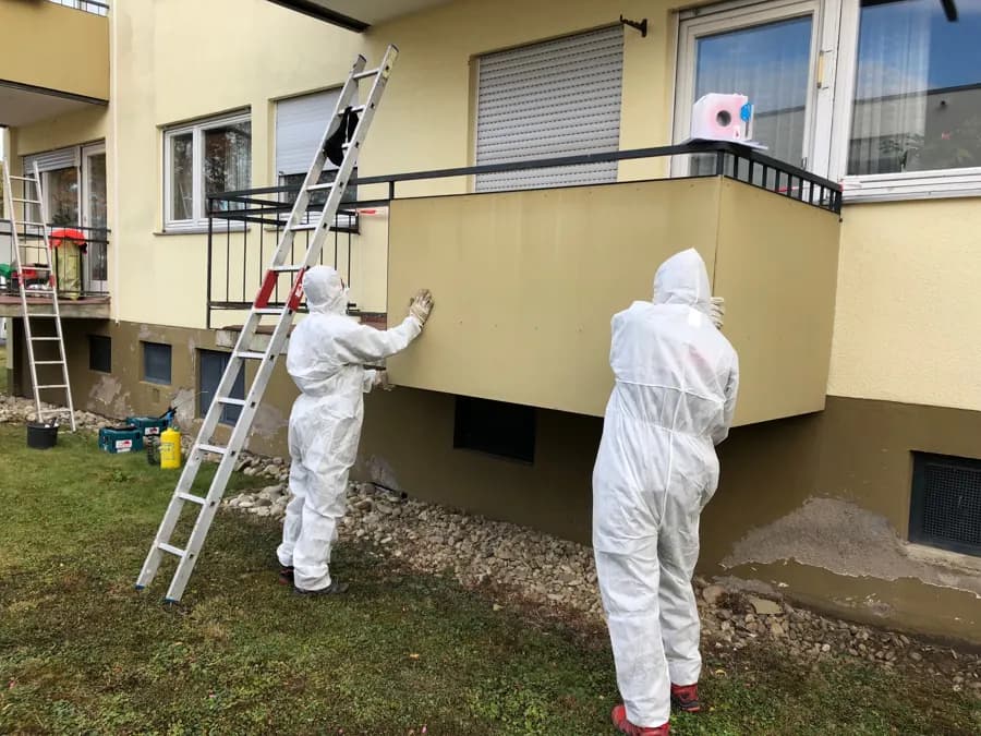 Zwei Mitarbeiter in Schutzanzügen an einem Balkon