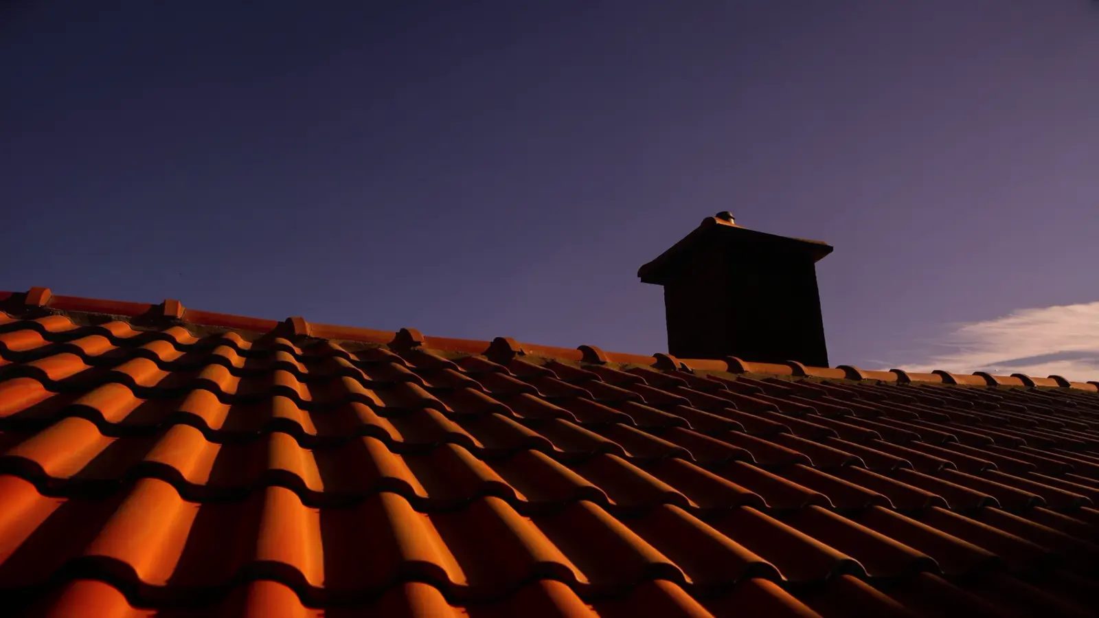 Ziegeldach neben einem Kamin, über das das Licht von der Blauen Stunde zum Morgenlicht wandert